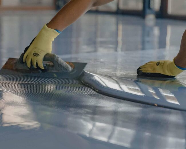 Aplicación de impermeabilización con llana - Tech Deck Flooring Operario aplicando recubrimiento impermeabilizante con llana dentada